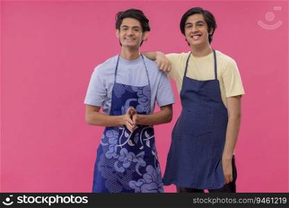 Two teenage boys in chef apron standing together against pink background