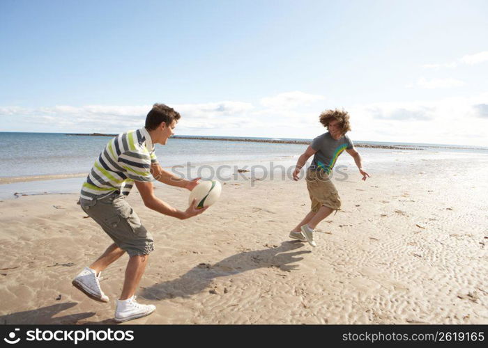 Two Teenage Boys Playing Rugby On Beach Together