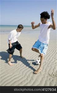Two teenage boys playing with a soccer ball on the beach