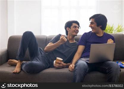 Two teenage boys using laptop on sofa in living room