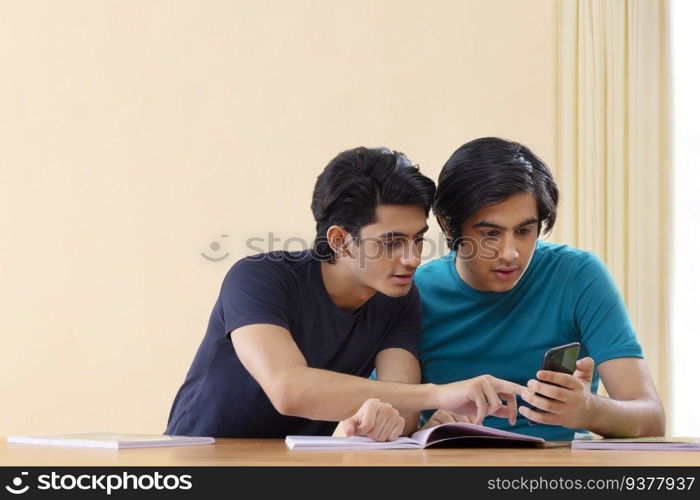 Two teenage boys using smartphone while studying together at home