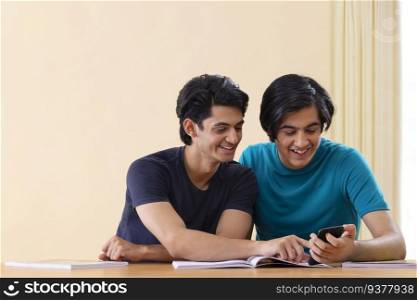 Two teenage boys using smartphone while studying together at home