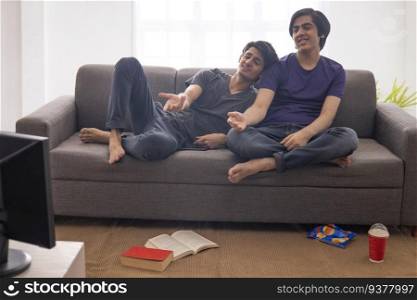 Two teenage boys watching TV and gesturing together while sitting on sofa in living room