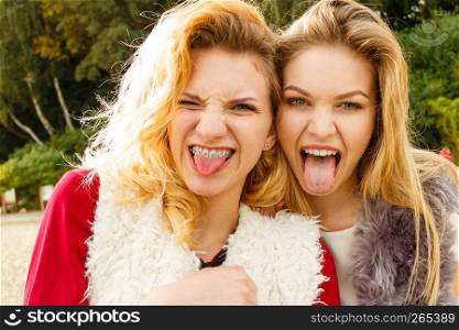Two teenage crazy fashionable women having fun fooling around smiling with joy, one sticking tongue out.. Two crazy women having fun outdoor