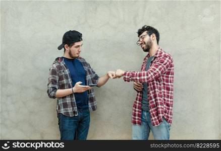 Two teenage friends greeting each other by fist bumping outdoors. Two smiling young guys bumping fists near a wall. Concept of two smiling friends bumping fists friendly