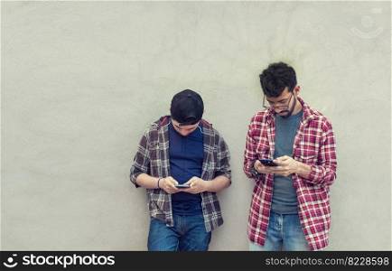 Two teenage friends on a wall checking their cell phones, Two friends leaning on a wall texting on their phones. Friend showing cell phone to his friend, Smiling friends checking cell phones