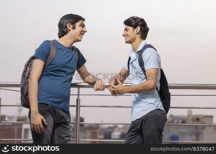 Two teenage friends talking while standing together by railing