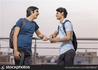 Two teenage friends talking while standing together by railing