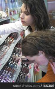 Two teenage girls bend over a display of make-up in a grocery store
