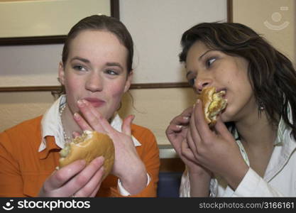 Two teenage girls in a fast food restaurant eating hamburgers