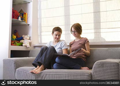 Two teenage girls looking at photo album on sofa