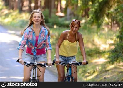 Two teenage girls riding their bikes laughing enjoy summer sport