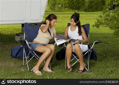 Two teenage girls sitting in armchairs and reading a magazine