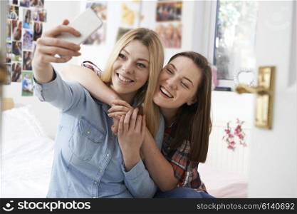 Two Teenage Girls Taking Selfie In Bedroom At Home