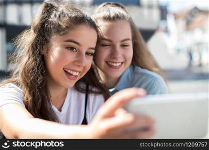Two Teenage Girls Taking Selfie On Mobile Phone Outdoors