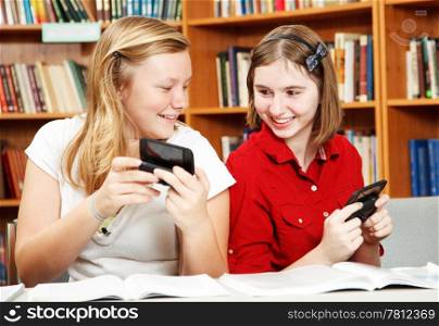Two teenage girls texting in school, instead of studying.