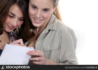 Two teenage girls writing on note pad