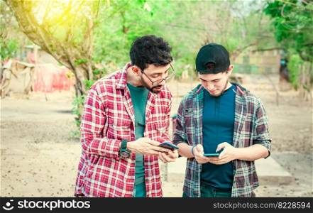 Two teenage guys pointing and checking their cell phones, Two friends looking at the content of their cell phone. Friend showing cell phone to his friend, Smiling friends checking cell phones