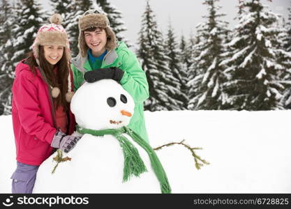 Two Teenagers Building Snowman On Ski Holiday In Mountains