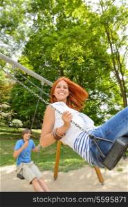 Two teenagers on swing playground in park smiling at camera