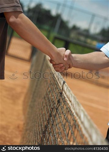 Two tennis players shaking hands over a net