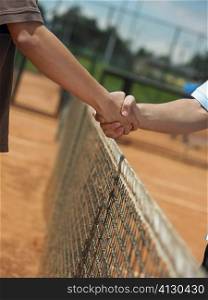 Two tennis players shaking hands over a net
