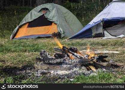 Two tents in forest. Fire on foreground