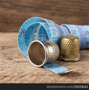 two thimble and measuring tape on a wooden background