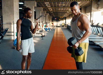 Two tired athletes doing exercise with dumbbells, training in gym. Fit workout in sport club, healthy lifestyle, fitness. Two tired athletes doing exercise with dumbbells