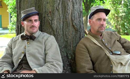 Two tired Civil War soldiers rest by tree