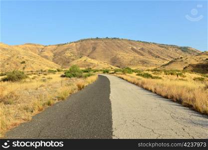Two-tone road in the Golan Heights. A yellow withered grass and blue sky.