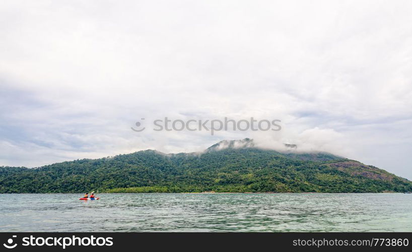 Two tourists are kayaking in the sea, surrounded by beautiful nature in the morning with clouds and fog covering Ko Adang island is the background, Tarutao National Park, Satun, Thailand. Two tourists are kayaking in the sea at Ko Adang island