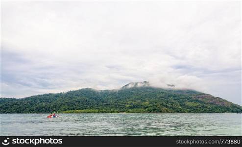Two tourists are kayaking in the sea, surrounded by beautiful nature in the morning with clouds and fog covering Ko Adang island is the background, Tarutao National Park, Satun, Thailand. Two tourists are kayaking in the sea at Ko Adang island