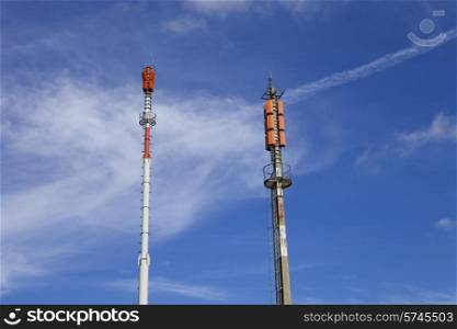 Two towers of communications with different antennas under blue sky.