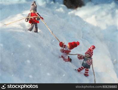 Two toy little man holding on to a rope, rescue scene in the winter in the fall in the open with the snow-capped mountains