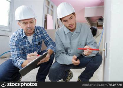 two tradesman crouched with clipboard