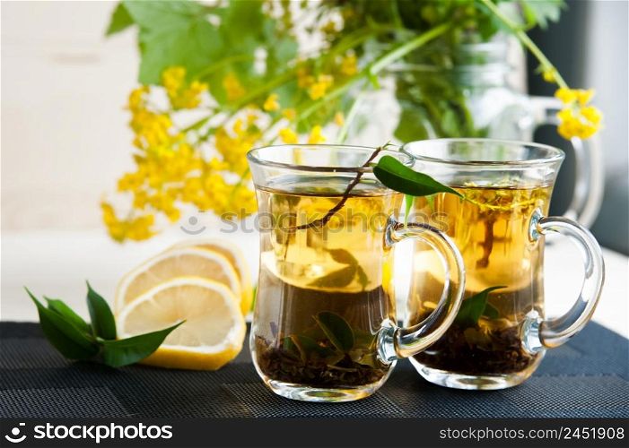 Two transparent cups with tea. Green, black, herbal, jasmine tea with lemon and ginger. Theme of tea. Cooking, tea packing, food production, restaurant business