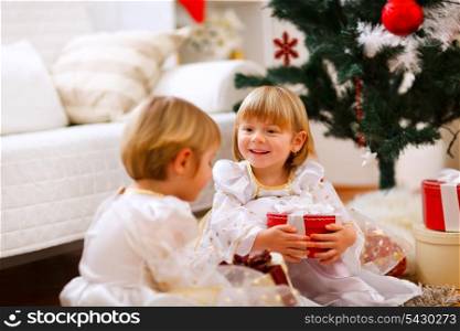 Two twins girl sitting with presents near Christmas tree&#xA;