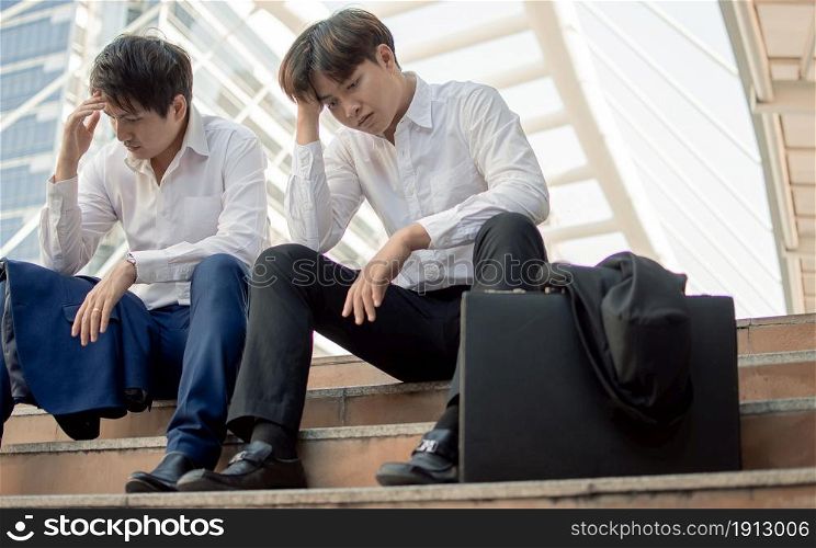 Two unemployed business men or workers sitting beside street and being sad after losing their jobs. Social Issue and Unemployment Concept.