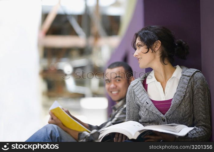Two university students leaning against a wall and holding textbooks