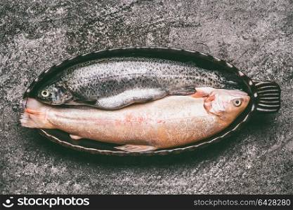 Two varieties of trout: brown trout and rainbow trout in baking bowl on gray granite table , top view. Healthy dieting and tasty cooking concept