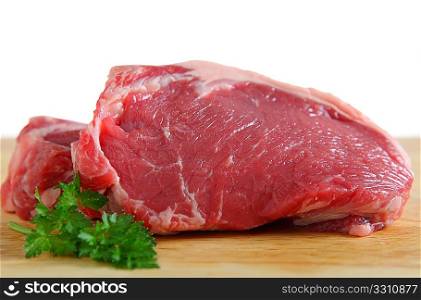 Two veal sirloin steaks on a wooden chopping board with a white background and a sprig of parsley