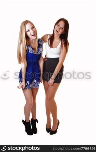 Two very pretty woman standing in the studio having fun and laughingin dresses and high heels, one blond and one brunette, over white.