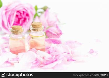 Two vials of rose essential oil, pink roses and rose petals isolated on a white background, with copy-space