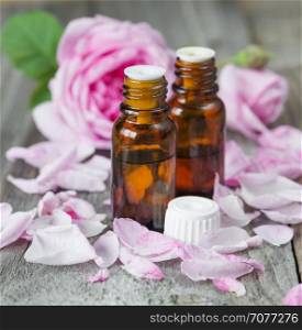 Two vials with essential oil and petals of pink roses on a wooden background
