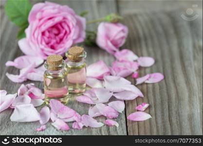 Two vials with essential oil and petals of pink roses on a wooden background
