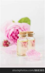 Two vials with essential oil and pink rose flowe are on a white background