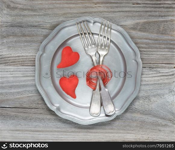 Two vintage fork and two scarlet hearts on an empty pink plate
