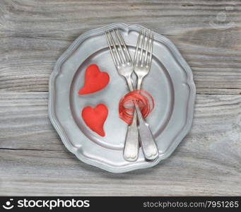 Two vintage fork and two scarlet hearts on an empty pink plate