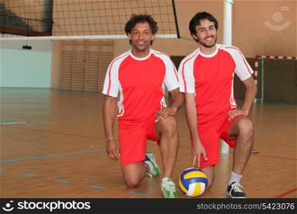 Two volleyball players kneeling with ball on indoor court